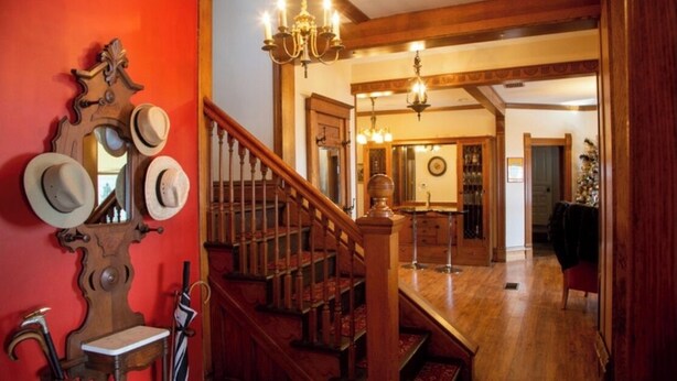 Una imponente escalera con barandillas de madera y una pared roja con un espejo y sombreros.