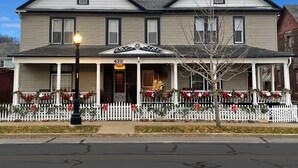Una casa de dos pisos con un porche, cerca viva blanca y decoraciones navideñas.