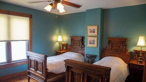 Un dormitorio con dos camas de madera, un ventilador de techo y una ventana con persianas.