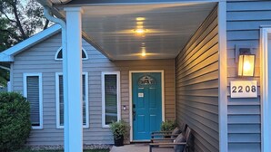 A house with a blue door, a porch with chairs, and a number sign '2208' on the wall.
