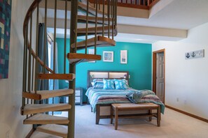Ein Schlafzimmer mit einer Holztreppe, einem Bett mit gestreifter Bettdecke und einer Wand in Türkis.