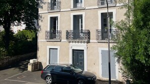 A multi-story building with balconies, a car parked in front, and a clear blue sky. - Apartment n°3 - T2 bedroom & separate bathroom (Lamalou-les-Bains)