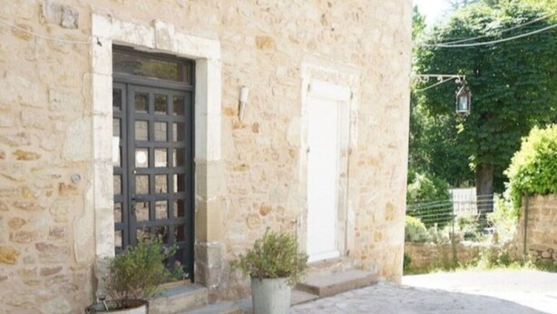 A stone building with a dark wooden door and white shutters, a paved courtyard, and potted plants. - Apartment n°3 - T2 bedroom & separate bathroom (Lamalou-les-Bains)