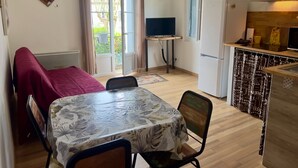 A compact living space with a dining area, kitchenette, and a view of the outdoors. - Apartment n°3 - T2 bedroom & separate bathroom (Lamalou-les-Bains)