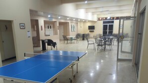Una habitación amplia con mesa de ping pong, varias sillas y mesas, presumiblemente un área de recreación.