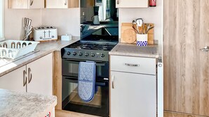 Eine kompakte Küche mit Gasherd, Backofen und kleinem Kühlschrank. Ein Toaster, ein Schneidebrett und ein Feuerlöscher sind an der Wand angebracht.