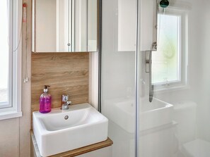 Un baño con lavamanos blanco, tocador de madera y ducha con cerramiento de vidrio.