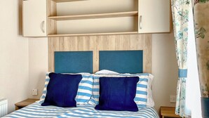 Ein Bett mit einer blau-weiß gestreiften Tagesdecke, zwei dunkelblauen Kissen und einem Kopfteil mit zwei Fächern.