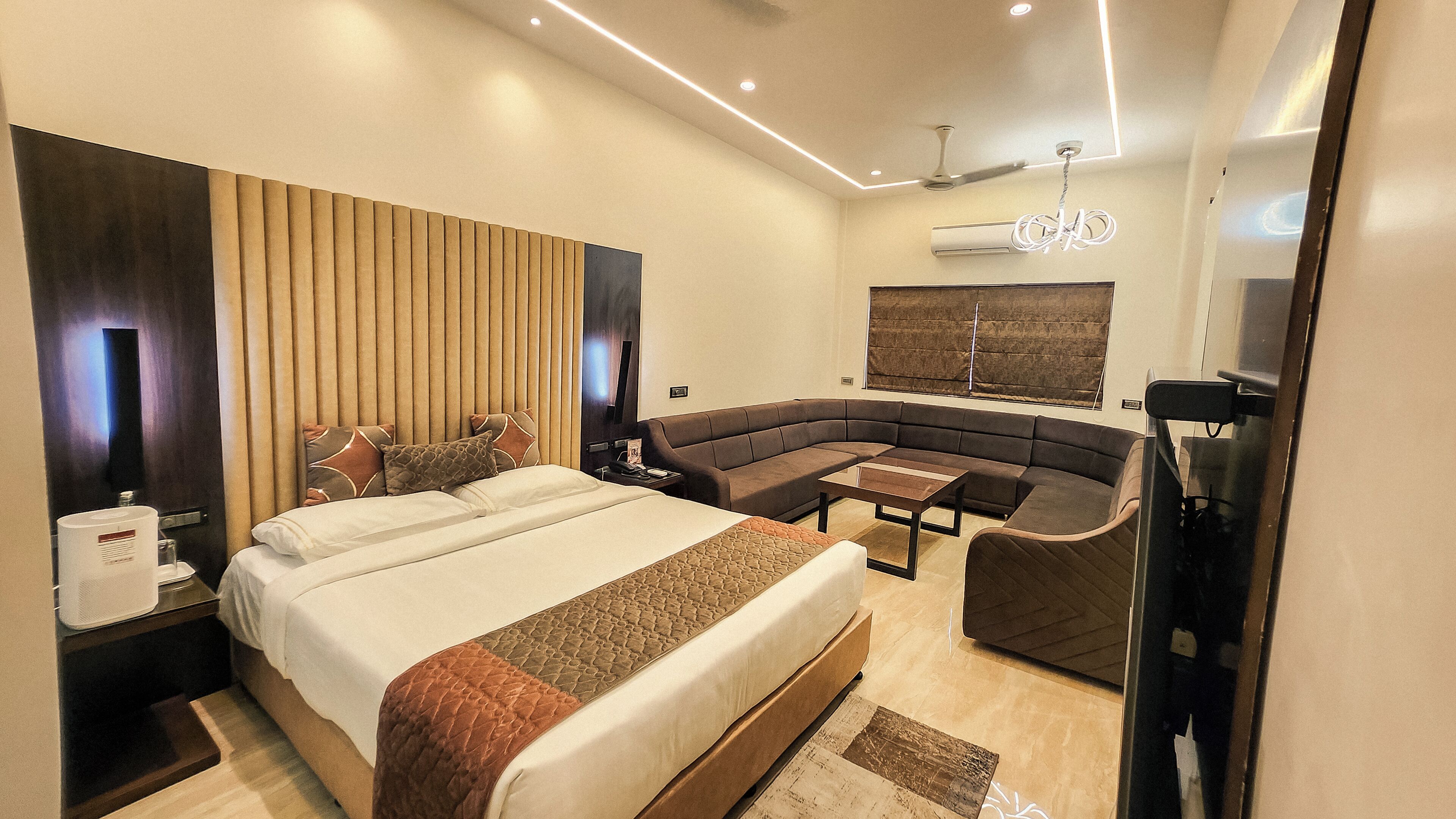 Una habitación de hotel moderna con una cama grande, un sofá curvo, una mesita pequeña y un ventilador de techo.