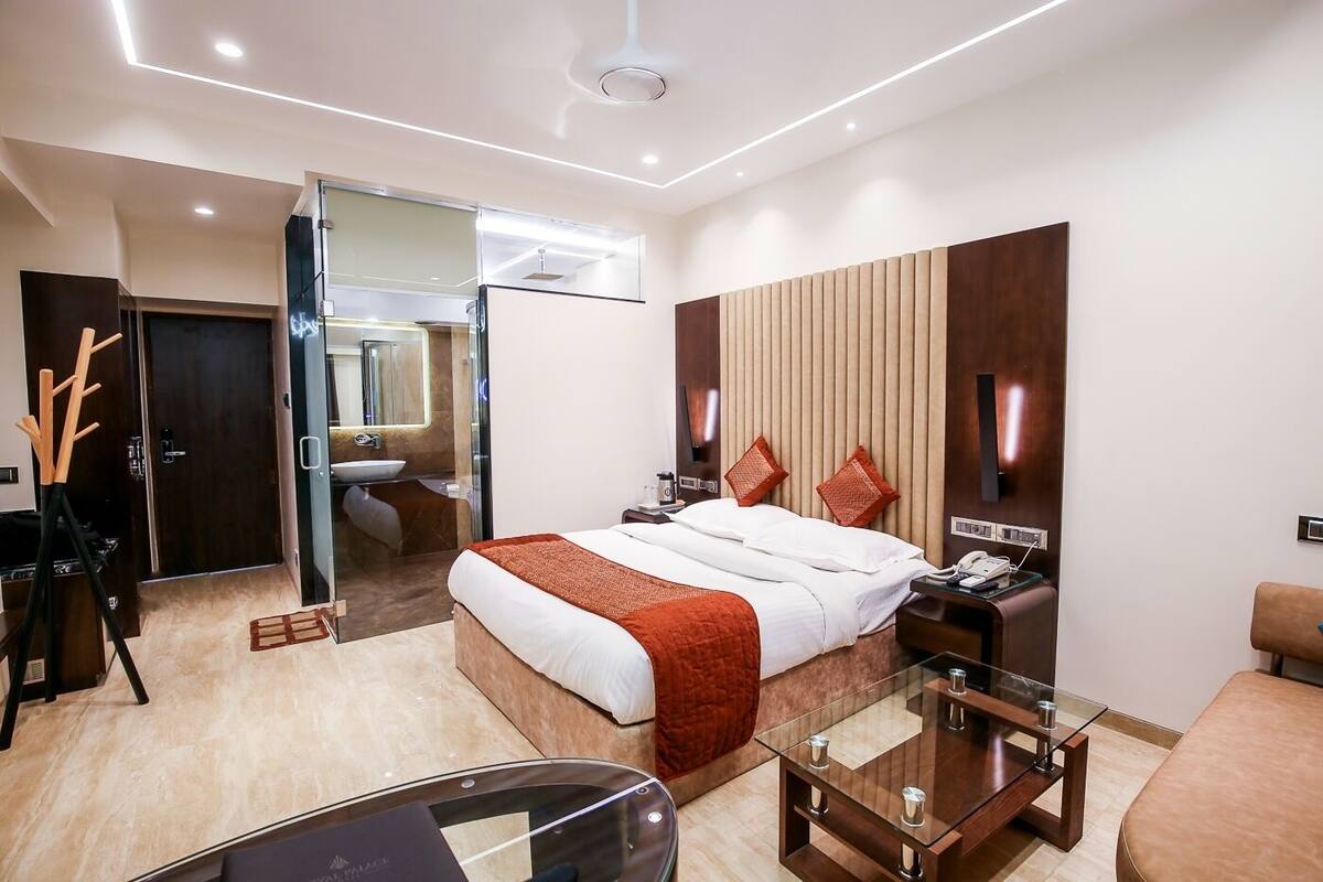 Une chambre d’hôtel moderne dotée d’un grand lit, d’une table basse en verre, d’une table de chevet, d’un bureau et d’une salle de bain visible à travers une porte en verre.