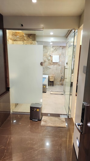A modern hotel lobby with a marble floor, a glass partition, and a small seating area with a chair and a table. - Hotel Royal Palace (Jalgaon)