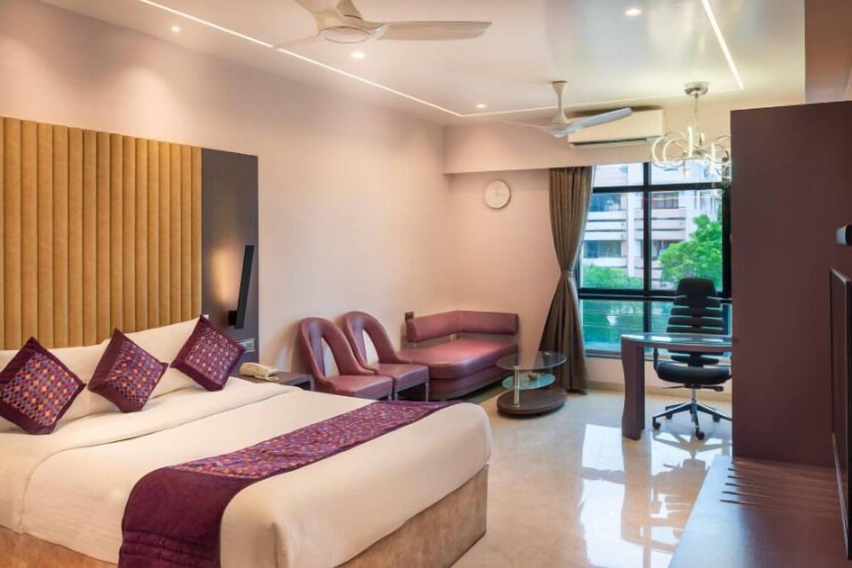 Une chambre d’hôtel avec un lit, deux fauteuils, un bureau et une télévision.