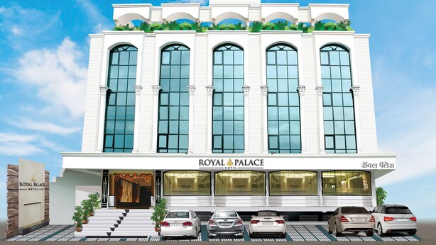 Hotelli nimeltä ”ROYAL PALACE HOTEL”, jossa on moderni julkisivu, suuret ikkunat ja useita autopaikkoja sisältävä pysäköintialue.
