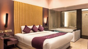 Moderni hotellihuone, jossa on suuri sänky, sängyn vieressä puhelin, yöpöytä, kylpyammeella varustettu kylpyhuone ja suuri peili.