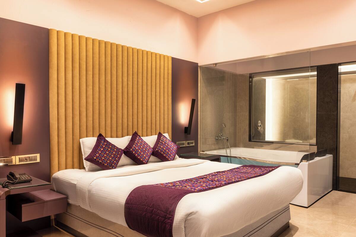 Une chambre d’hôtel moderne dotée d’un grand lit, d’un téléphone sur la table de chevet, d’une petite table de nuit, d’une salle de bain avec baignoire et d’un grand miroir.
