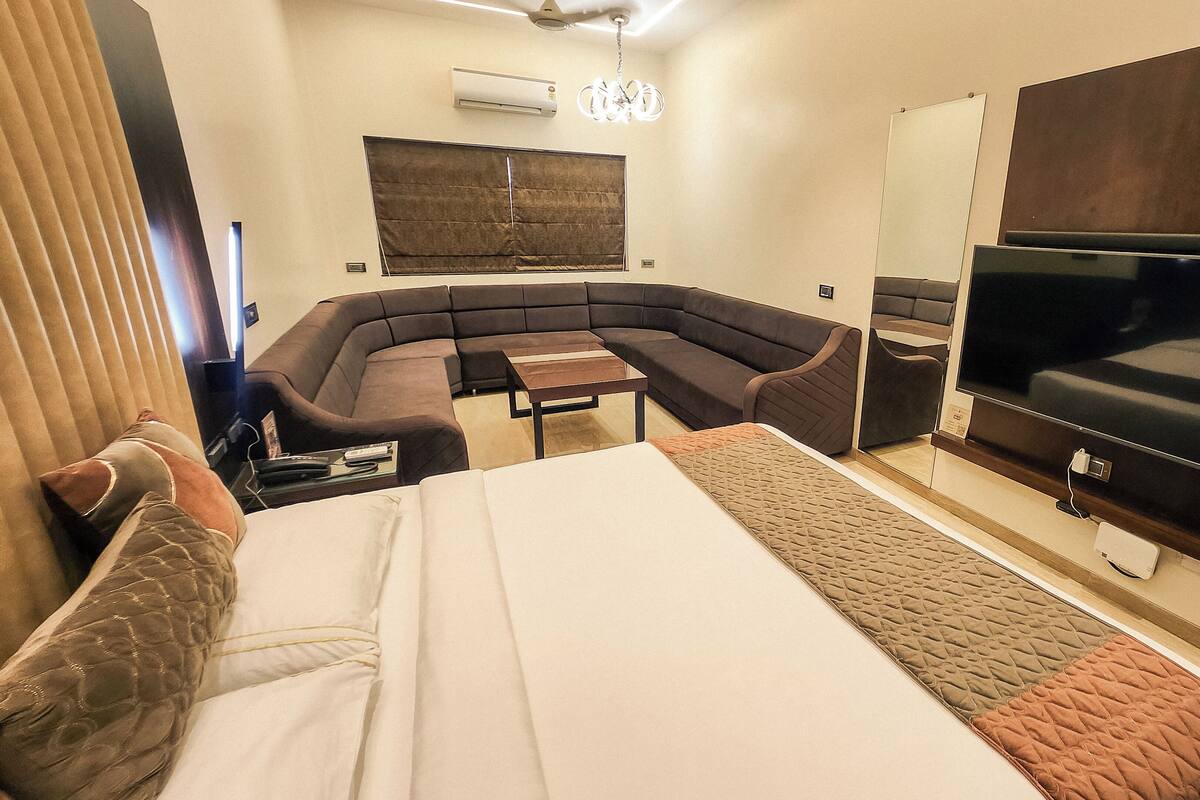 Une chambre d’hôtel moderne, dotée d’un grand lit, d’un canapé incurvé, d’une petite table, d’un téléviseur et d’un appareil de climatisation.