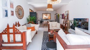 Una sala de estar moderna con un sofá, una mesa de centro y un televisor. En el fondo, se ve un comedor con una mesa y sillas.