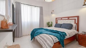 Un dormitorio con cama, mesita de noche, lámpara, cortinas y una lámpara colgante.