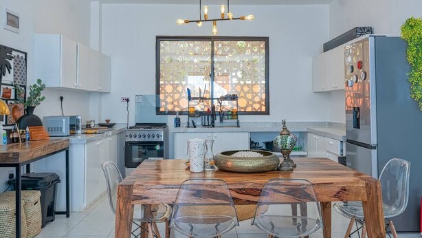 Una cocina moderna con armarios blancos, una mesa de comedor de madera y un ventanal con celosía decorativa.