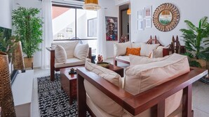 Una sala de estar moderna con un juego de sofá, una mesa de centro y lámparas colgantes de ratán. Hay plantas en macetas y obras de arte en las paredes.
