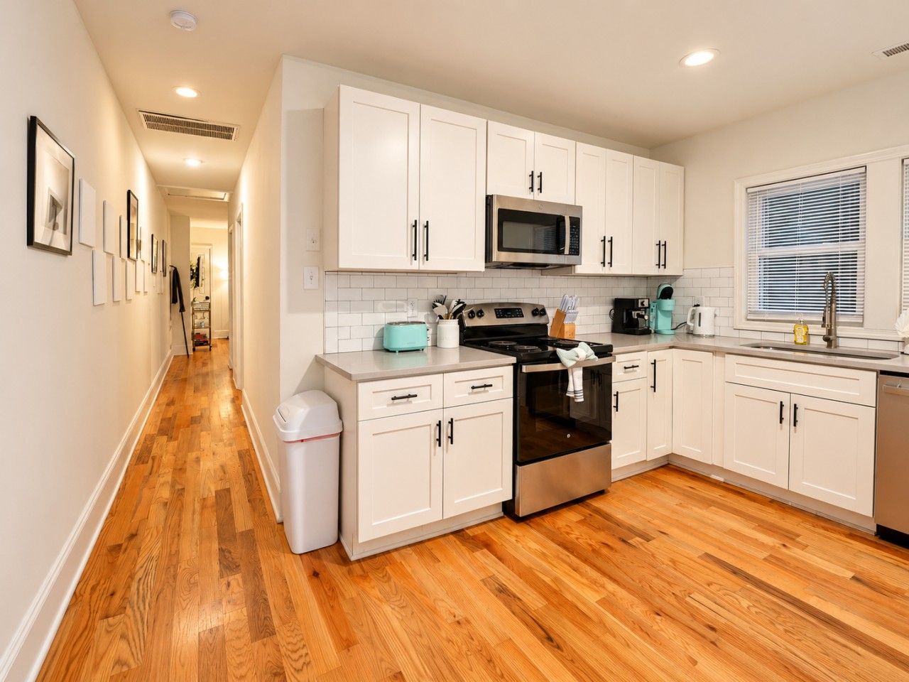 A kitchen with white cabinets, a stainless steel oven, a microwave, and a wooden floor.