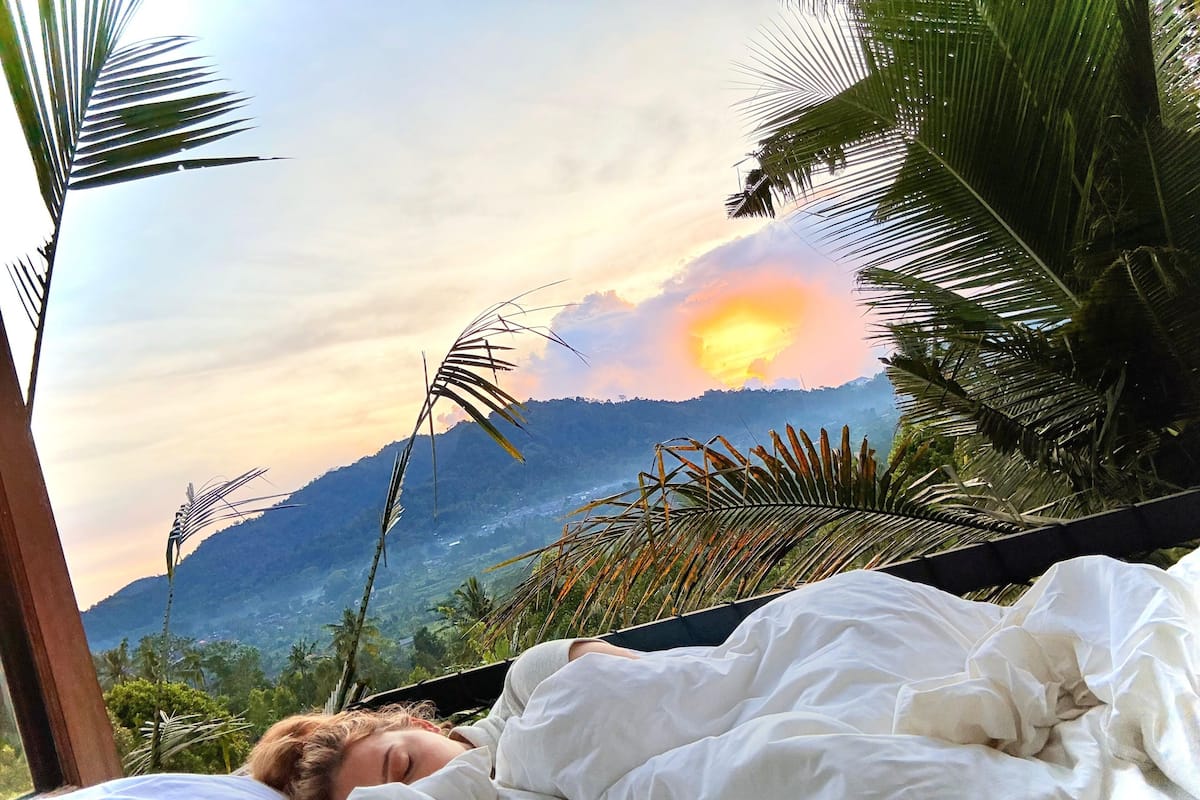 A person lying in a hammock with a view of mountains and a sunset.