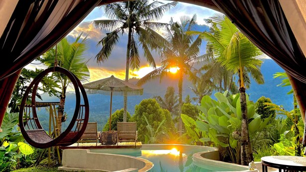 Un espace de détente circulaire avec une piscine, entouré d’une végétation luxuriante et de palmiers, le tout abrité par un toit de chaume.