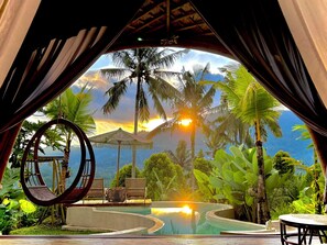 Un'area lounge circolare con piscina, immersa nel verde lussureggiante e palme, coperta da un tetto di paglia.