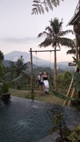 A couple on a swing overlooking a pool with a mountainous backdrop.
