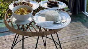 Une table à manger, dressée avec des assiettes remplies de nourriture, et une vue sur un paysage luxuriant, visible à travers une porte vitrée.