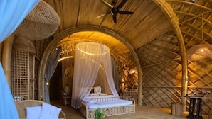 Une pièce accueillante, ouverte sur l’extérieur, avec un lit, une chaise en osier et une petite table.