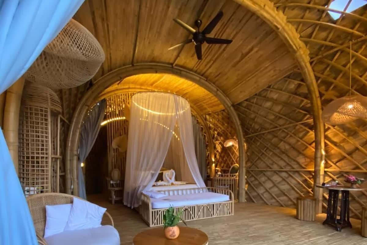 A cozy, open-air room with a bed, a wicker chair, and a small table.