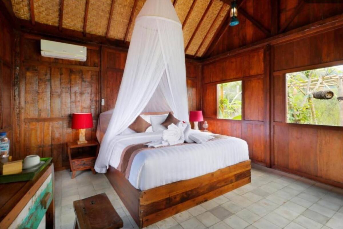 A wooden room with a bed, a nightstand, a table with bottles, and a window.