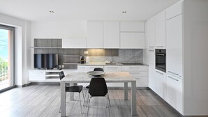 Une cuisine moderne avec des meubles blancs, un plan de travail en marbre et un coin repas comprenant une table et des chaises.