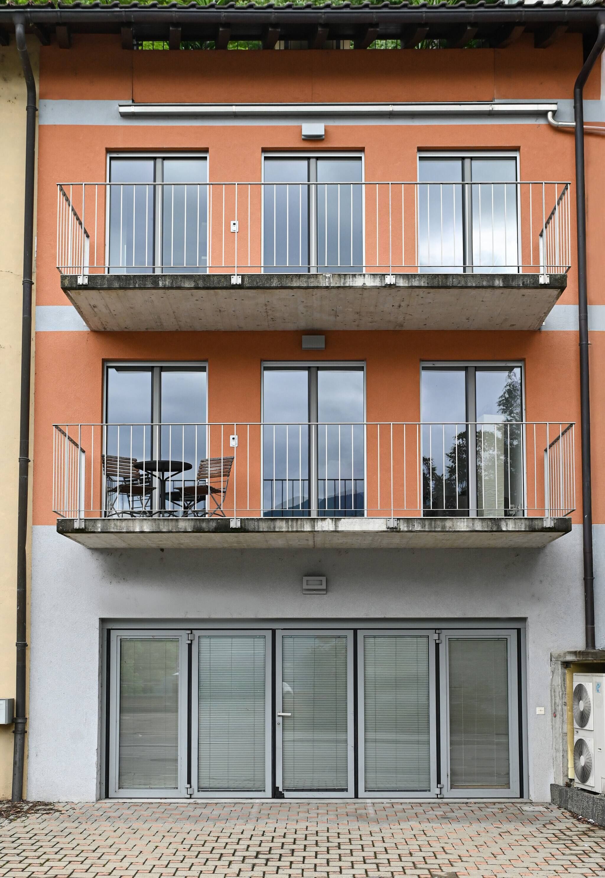 Un immeuble de deux étages doté d’un balcon à l’étage supérieur, où se trouvent une table et des chaises.