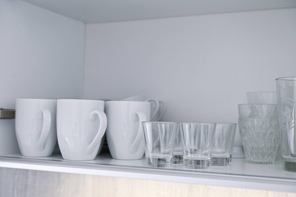 A shelf with white ceramic mugs and clear glass cups. - Lake View Suite 86 in Melide (Melide)