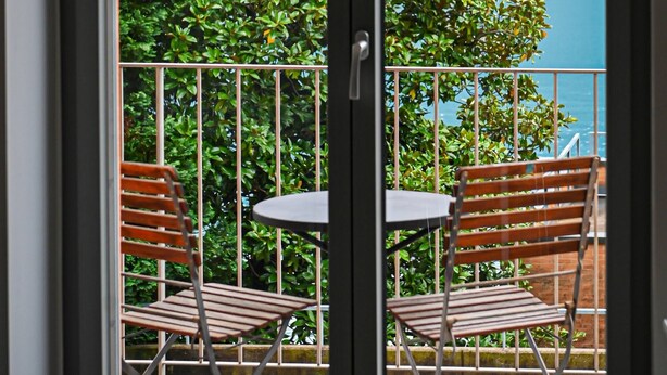 Un balcon avec deux chaises en bois et une petite table, d’où l’on peut admirer un lac et des montagnes.