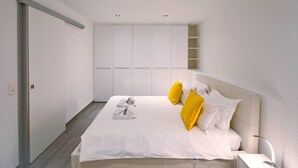 Une chambre à coucher avec un lit, du linge de lit blanc, une table de chevet, une lampe et une armoire.