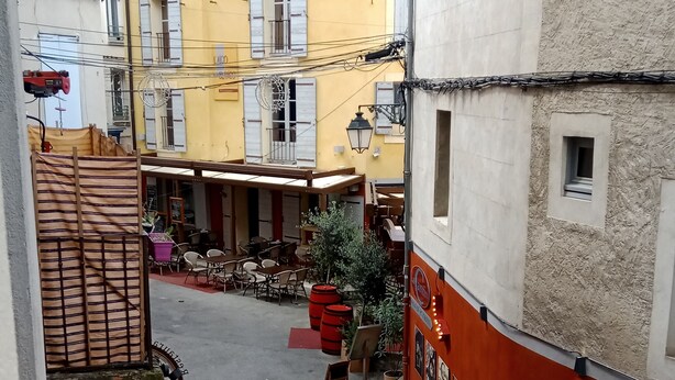 A narrow street with buildings on either side, outdoor seating, and a staircase leading to an upper level. - Apartment downtown Forcalquier (Forcalquier)