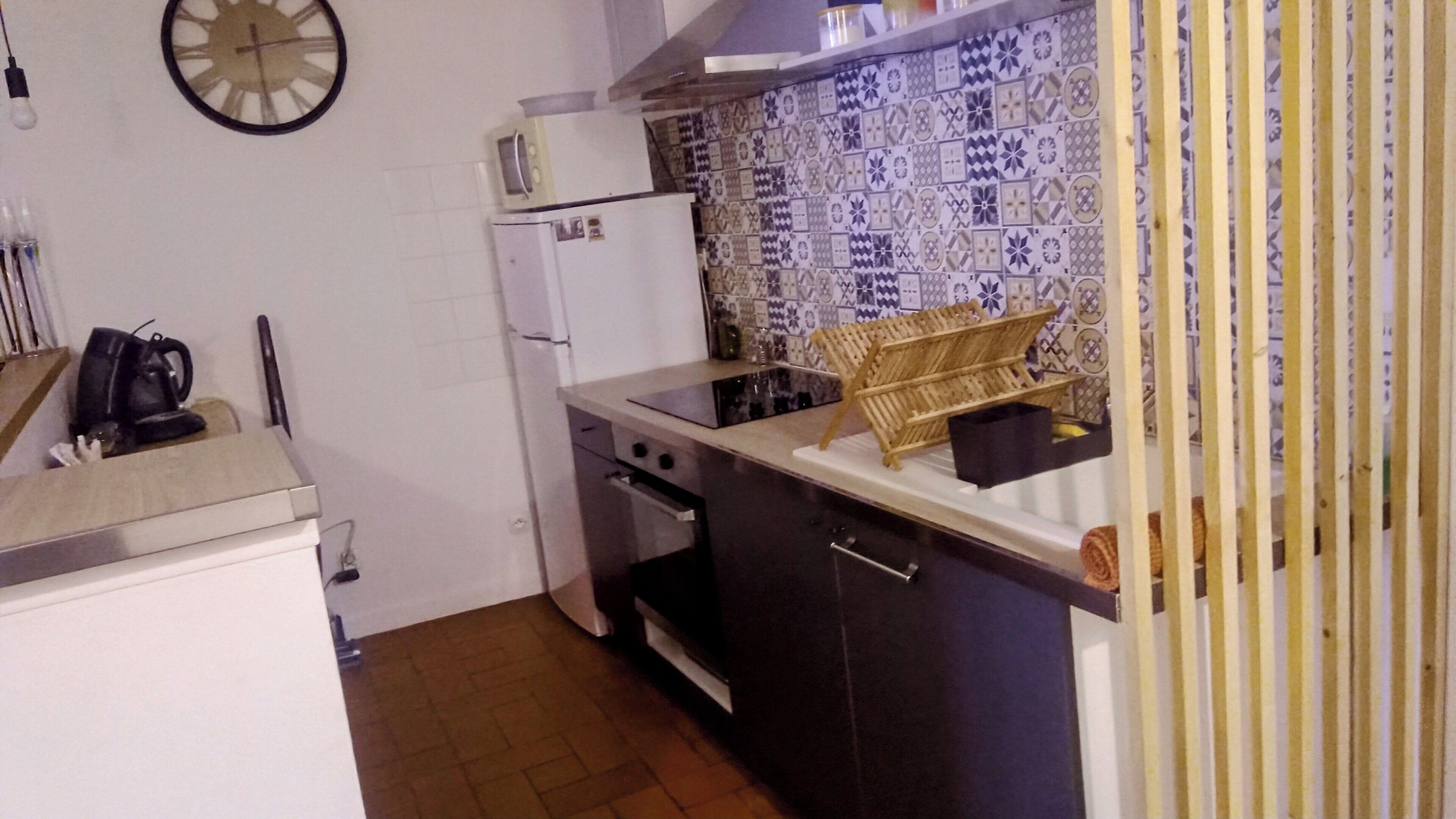 A compact kitchen with a refrigerator, stove, and a microwave. There is a sink with a modern faucet, and a patterned backsplash.