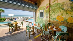 Een restaurant aan het strand met terras, een zwembad en een muurschildering van tropische bloemen.