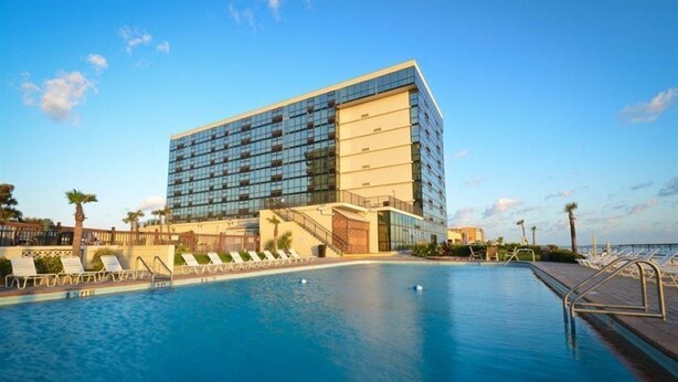 Een modern hotel met een groot zwembad, ligbedden en een helder uitzicht op de oceaan.