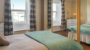 Une chambre à coucher avec un lit, une commode, un miroir et une fenêtre avec des rideaux.