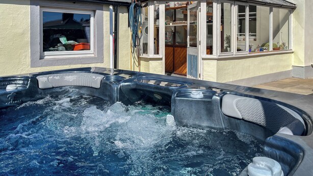 Un bain à remous dans un jardin, avec une maison en arrière-plan.