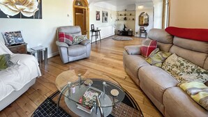 Un salon spacieux avec un fauteuil gris, un canapé beige et une table basse en verre.