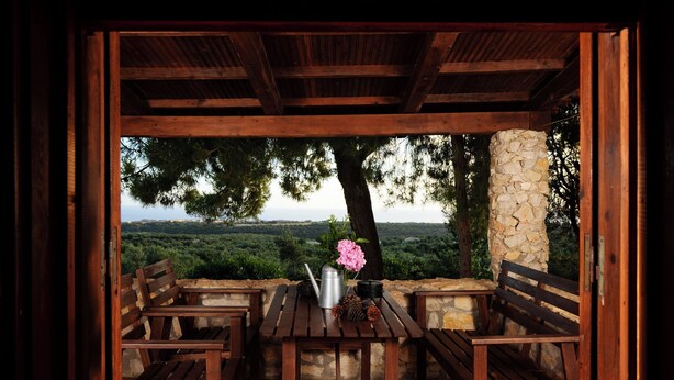 A wooden pergola with a table and benches, overlooking a scenic landscape with trees and a stone pillar. - Cozy 1-bedroom apartment overlooking the Ionian sea. (Tragana)