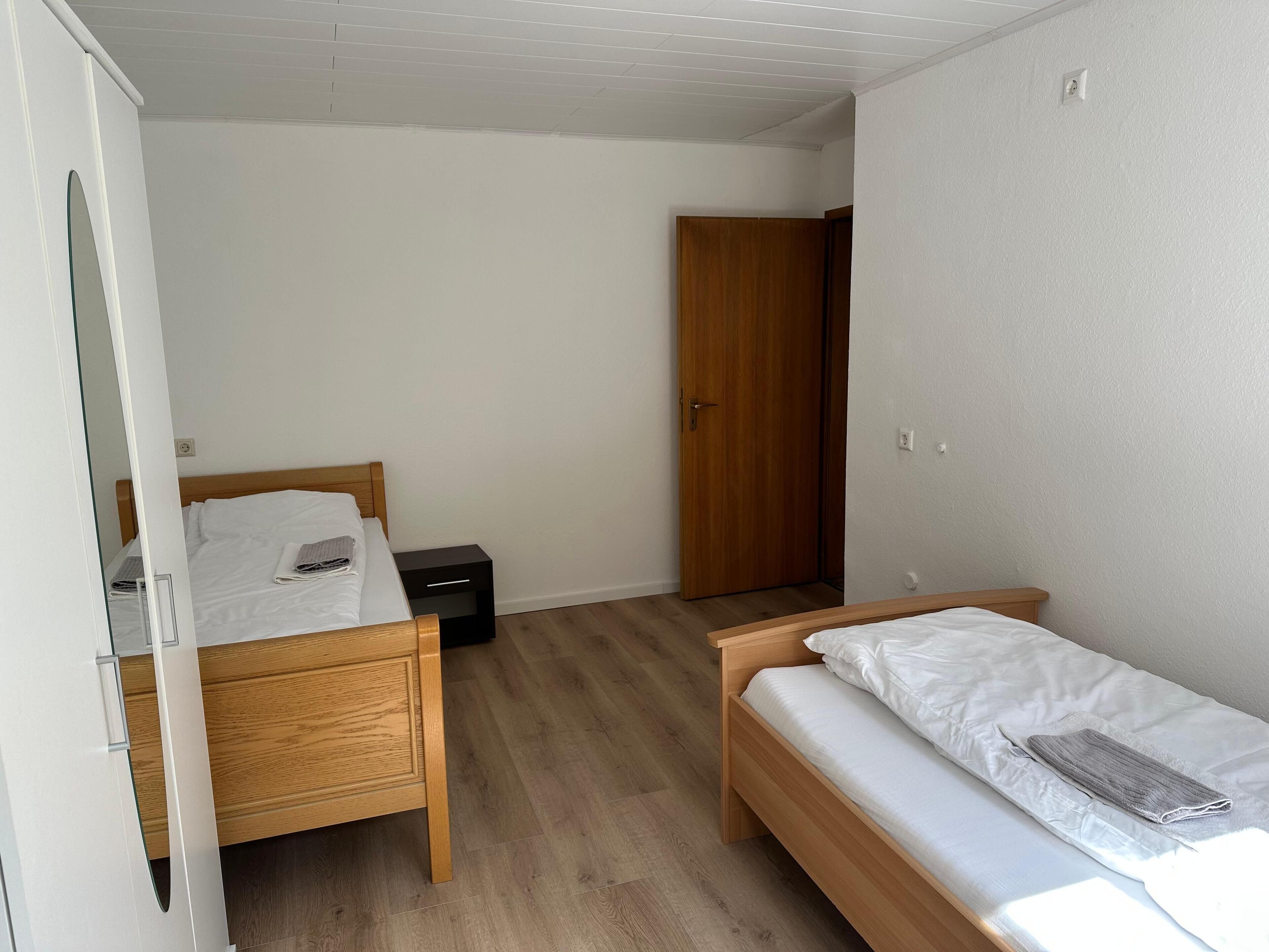 A small, clean room with a wooden bed, a nightstand, and a wardrobe.