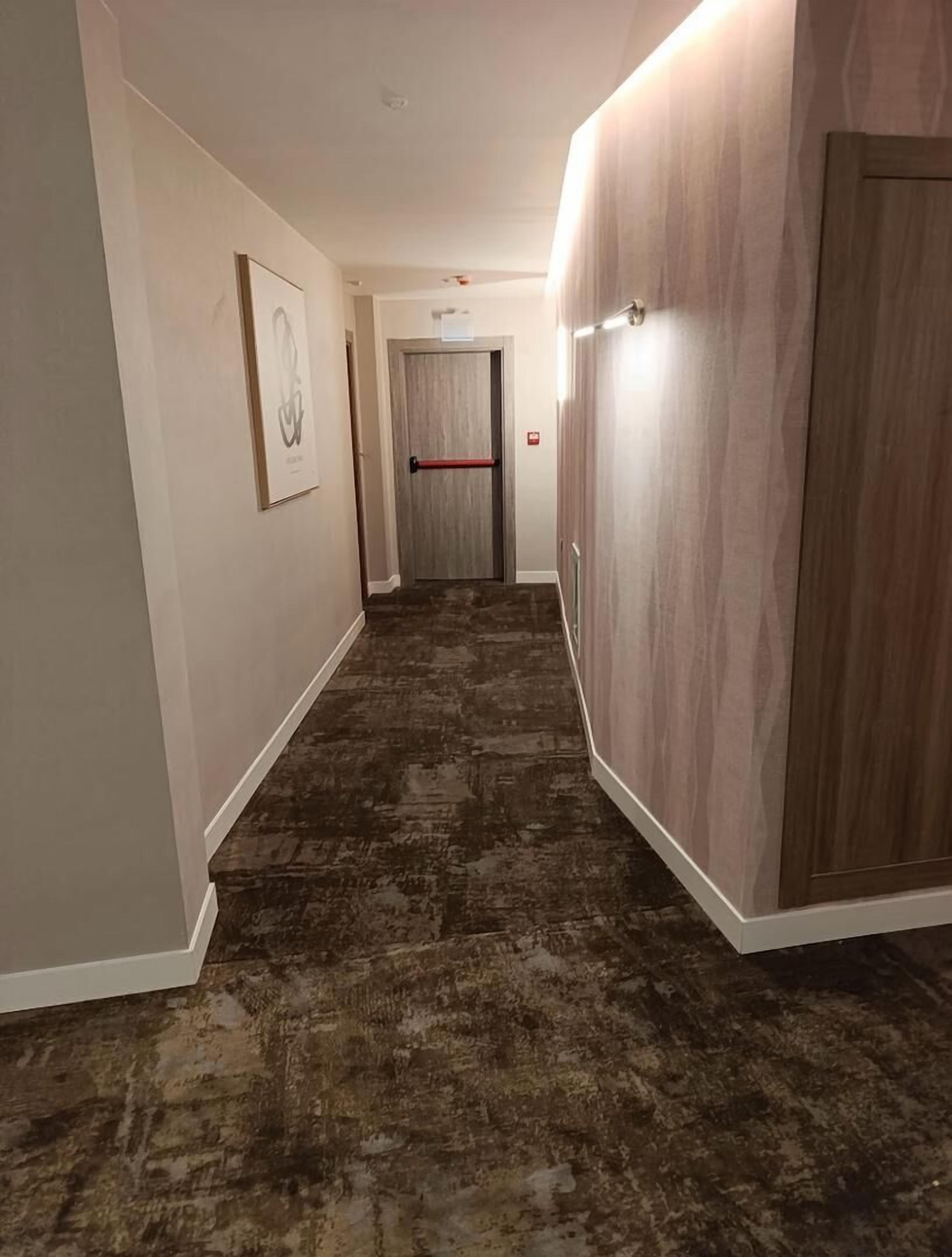 Un pasillo con alfombra estampada, paredes de madera y una puerta con picaporte rojo.