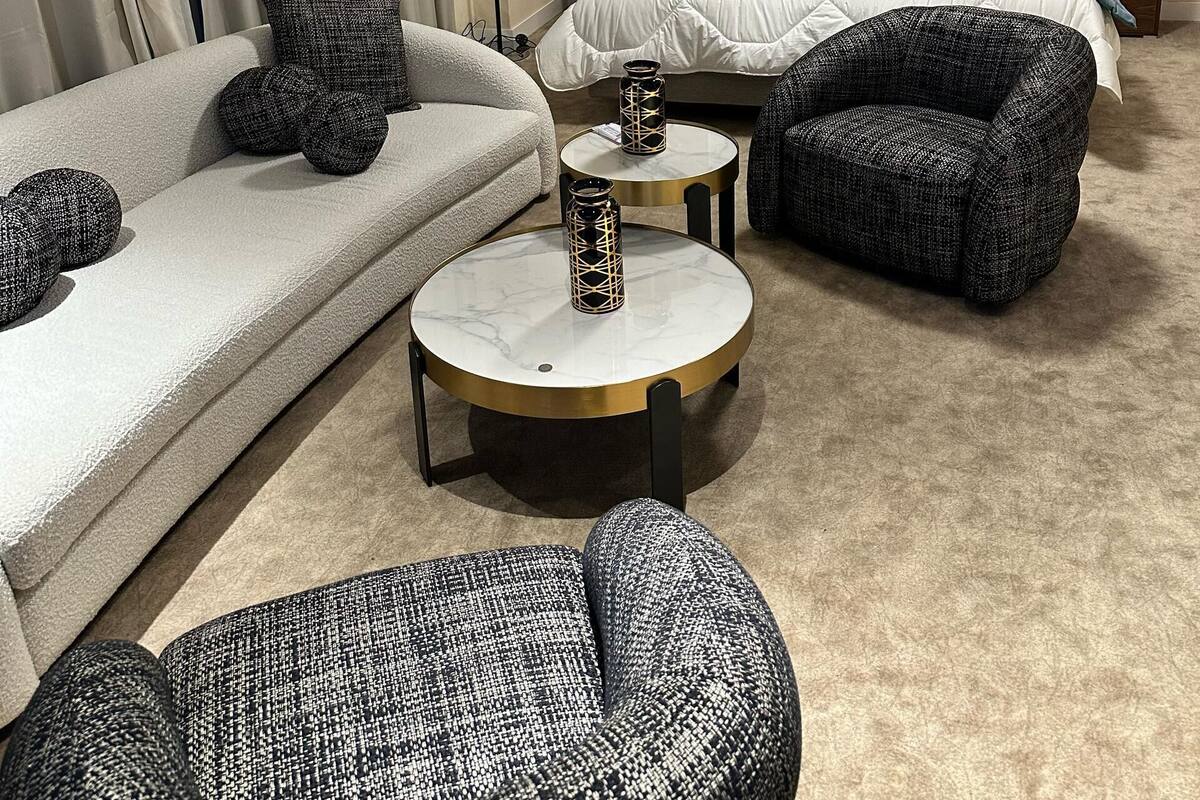 A modern hotel room with a large bed, a sofa, two armchairs, and a small round table.
