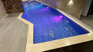 Ein Innenpool mit einer gefliesten Kante, umgeben von Marmorwänden und einer Wand aus Naturstein.